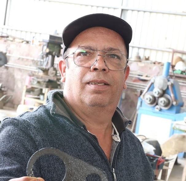 Una persona con gorra y gafas se encuentra en un taller sosteniendo una herramienta. Al fondo se ven varios equipos industriales.
